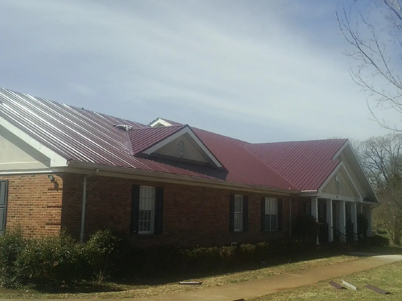 Red metal roof with gabled entries on a long brick building, from a Hail Damage Roof Repair job in Millbury