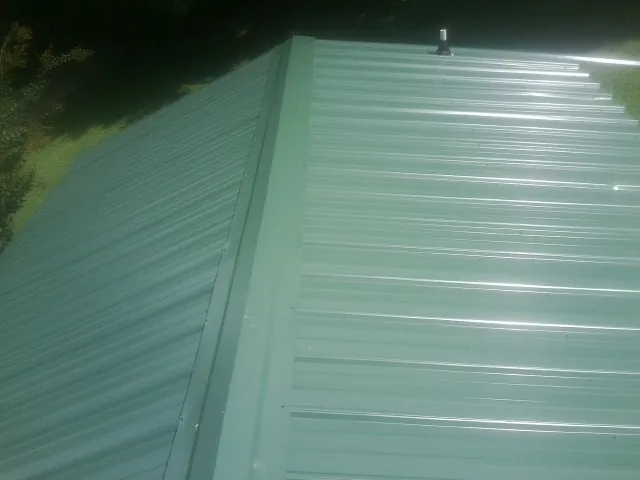 New green metal panels meeting at the ridge of a roof — Flat Roof Repair work by our crew in Millbury