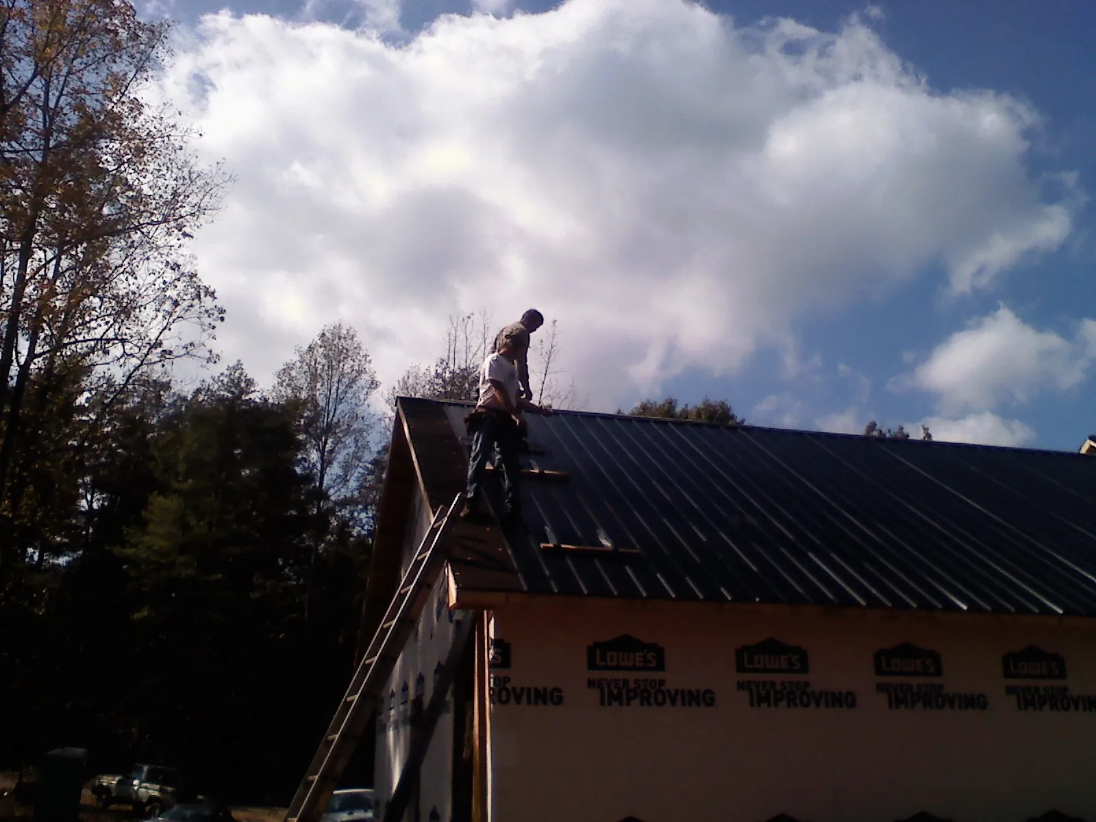 Roofer fastening dark metal panels high against a cloudy sky, from a Roof Inspection job in Millbury