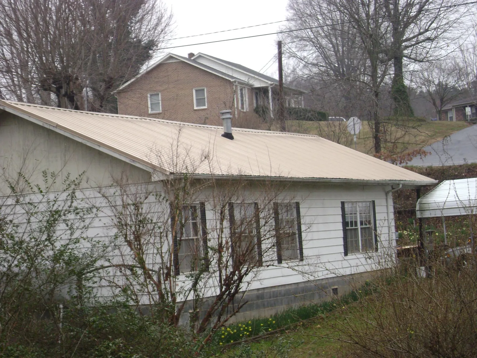 Tan metal roof on a white sided house set into a hillside — Commercial Roofing by Roofing Brothers in Millbury